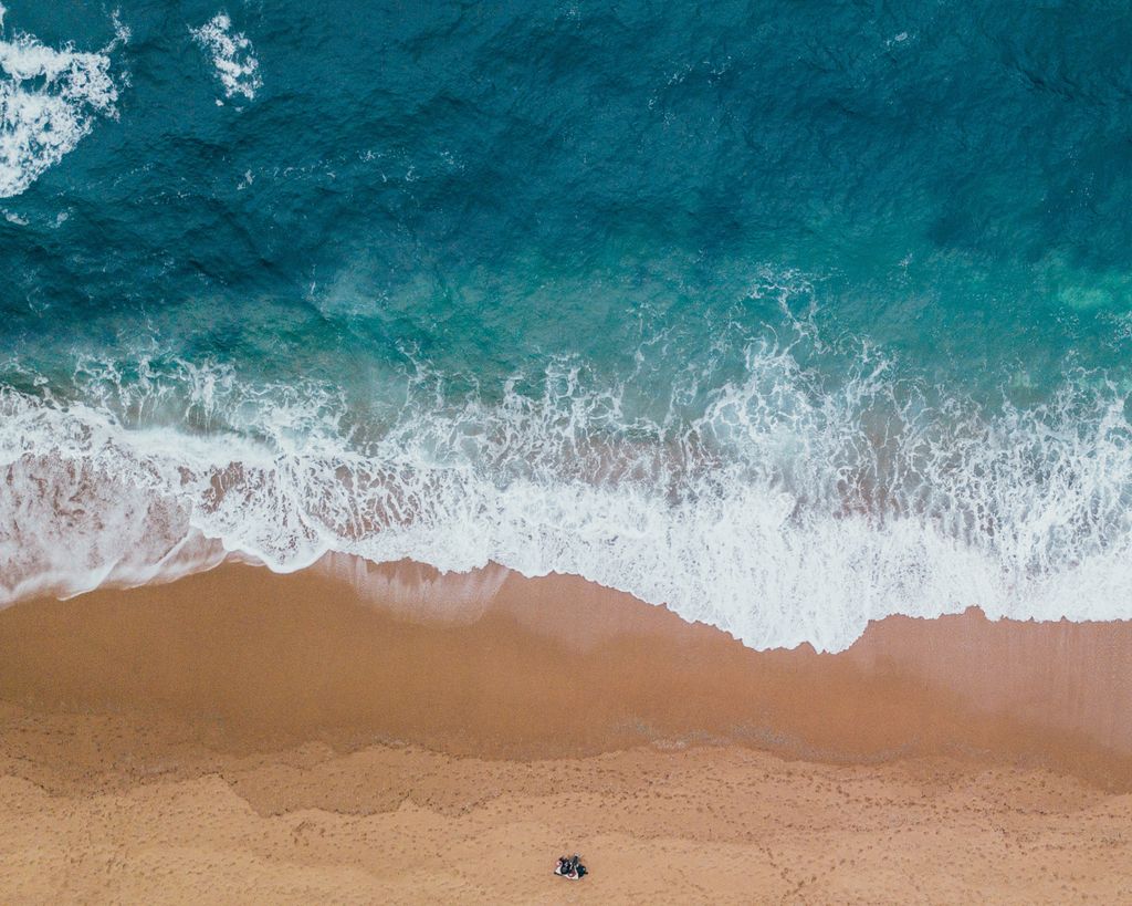 A stunning aerial shot capturing waves gently crashing onto a sandy beach, showcasing the beauty of the ocean.